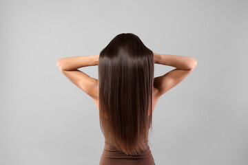 Hair styling. Woman with straight long hair on grey background, back view