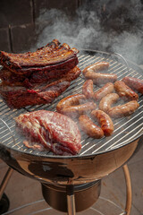 Beef steak and pork meat on the barbecue. Grilled meat surrounded by smoke. Food concept. High angle view of meat on barbecue grill