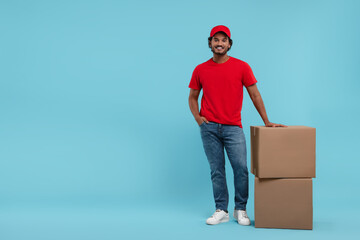 Happy courier with parcels on light blue background, space for text