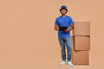 Happy courier with clipboard and stack of parcels on light brown background, space for text