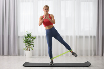 Athletic woman doing exercise with fitness elastic band on mat at home