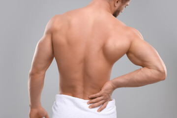 Man suffering from back pain on grey background, back view
