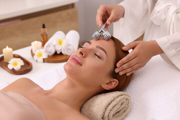 Obraz na płótnie Canvas Young woman receiving facial massage with metal roller in beauty salon, closeup