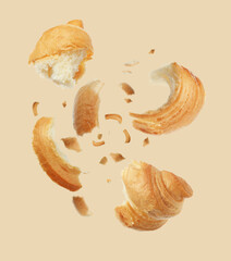 Pieces of delicious fresh croissant falling on beige background
