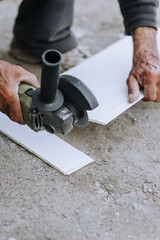 A man, a worker in an outdoor workshop, cuts off a plastic material for insulation with a grinder, an electric cutter.