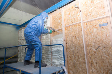 Insulation of walls with foam, energy and heat saving of walls, worker treats walls with foam