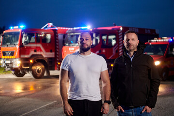 Group of firefighters, dressed in civilian clothing, stand in front of fire trucks during the...