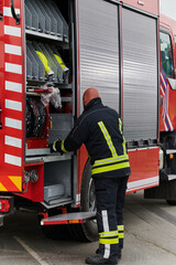 Naklejka premium A firefighter meticulously prepares a modern firetruck for a mission to evacuate and respond to dangerous situations, showcasing the utmost dedication to safety and readiness in the face of a fire