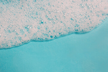 Close-up of shampoo or soap foam on blue surface with copy space, abstract background,