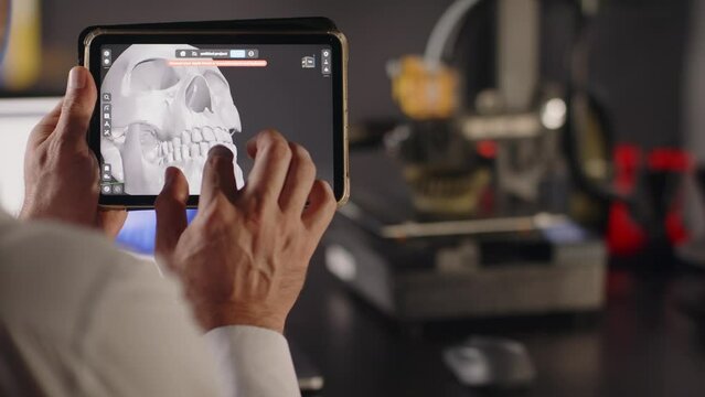 A man graphic designer holds in hands and uses a tablet to view 3d model of a human skull with teeth. The concept of bioprinting organs for transplants on 3d printers. The future of medicine. Close up