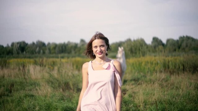 beautiful woman walks through a field in a pink dress and enjoys nature, a horse in the meadow.