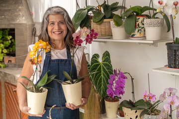 Mature woman happy surrounded by plants holding two orchids - Powered by Adobe