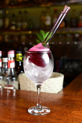 refreshing alcoholic drink with berries, ice vodka and gin, lemon peel served in glass cup on the counter on blurred background