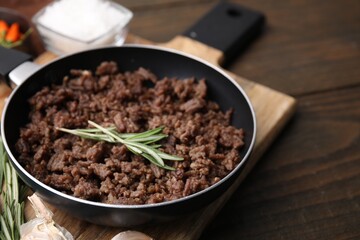 Fried ground meat in frying pan and rosemary on wooden table, closeup. Space for text