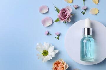 Bottle of cosmetic serum, beautiful flowers and petals on light blue background, flat lay. Space for text