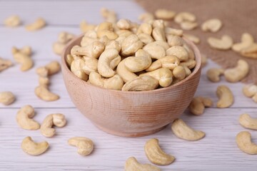 Tasty cashew nuts in bowl on white wooden table, closeup