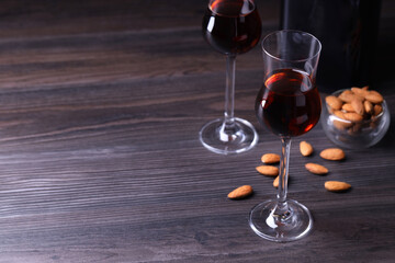 Liqueur glasses with tasty amaretto and almonds on wooden table, space for text