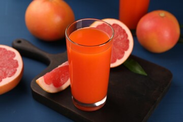 Tasty grapefruit juice in glass and fresh fruits on blue table, closeup