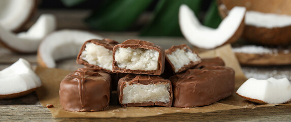 Delicious milk chocolate candy bars with coconut filling on wooden table, closeup. Banner design