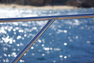 Macro of shiny metal rail on boat, ocean and rocky beach in background with bokeh - Powered by Adobe