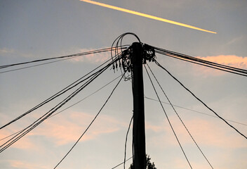 Lots of electrical cables on a pole during sunset with an airplane in the background. Electricity....