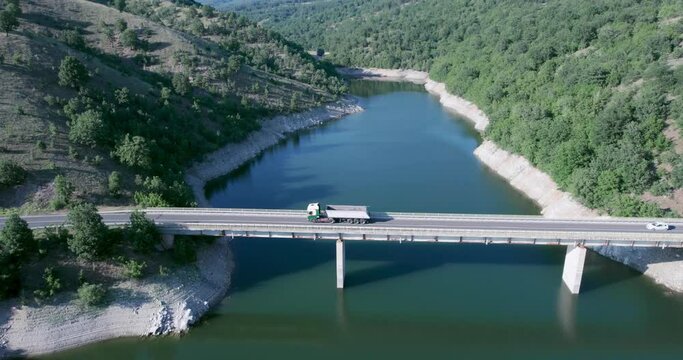 Cargo empty truck drives on river, lake bridge in early hours of the morning, aerial drone shot