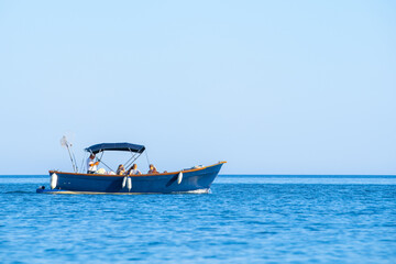 Company of tourists on recreational fishing boat with awning on sunny summer day in middle of open sea against sky. Family rented pleasure vessel excursion, fishing. Weekend boat trip, corporate rest
