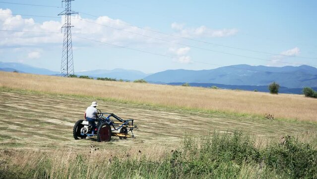 Agricultural tractor cuts and turns a field of alfalfa for drying with swather mower, slow motion