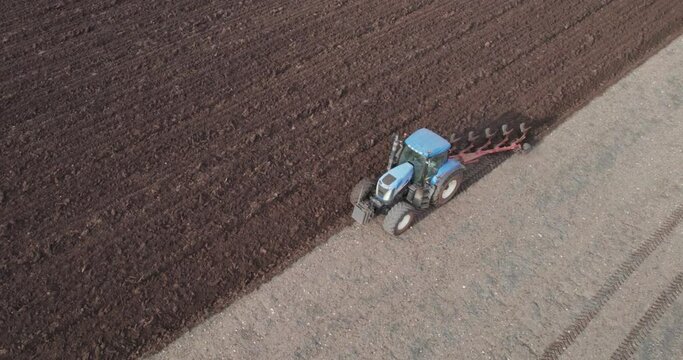 Large industrial tractor plowing soil on agriculture field in spring. Preparation for soybeen, wheet, rye seeding. Aerial shot