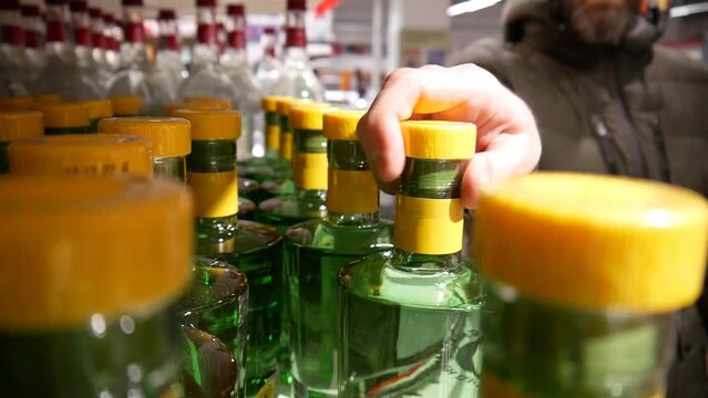 A man with a shopping cart takes a nice bottle of gin or absinthe in a supermarket