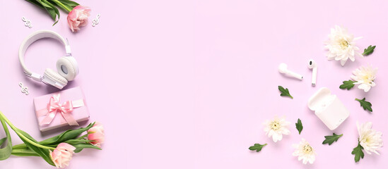 Modern headphones with earphones, gift and flowers on pink background with space for text