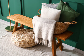Fototapeta na wymiar Basket with pillows and plaid on wooden bench near green wall in room
