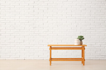 Wooden table with bonsai tree and decorative figure near white brick wall