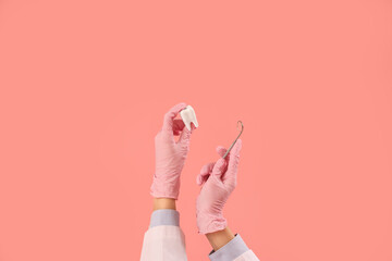 Female doctor's hands with dental mirror and tooth model on pink background