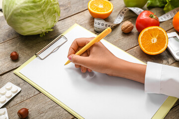 Female doctor's hand with blank clipboard, pen and healthy products on wooden background, closeup