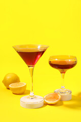 Glasses of Cosmopolitan cocktail with lemon on yellow background