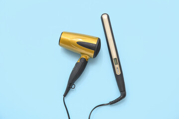 Hair dryer and flattening iron on light blue background, top view