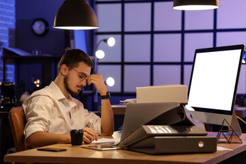 Tired young man with laptop, computer and folders working in office at night