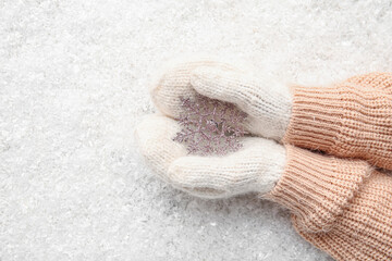 Female hands in warm mittens with decorative snowflake on snow