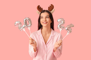 Beautiful young woman in striped pajamas and reindeer horns with air balloons in shape of figure...