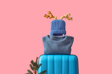 Suitcase with Christmas tree, deer horns and warm clothes on pink background. Winter vacation...