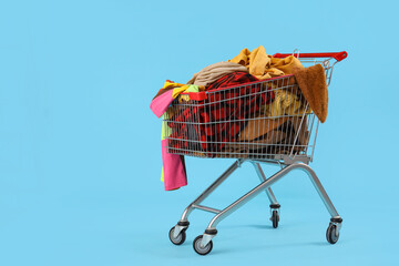 Shopping cart full of clothes on blue background