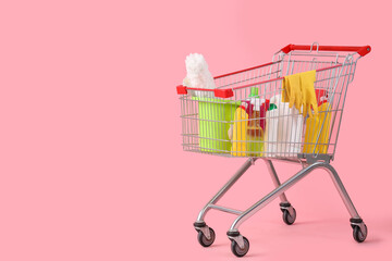 Shopping cart with cleaning supplies on pink background