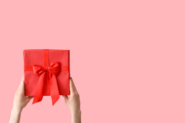 Female hands holding Christmas gift box on pink background