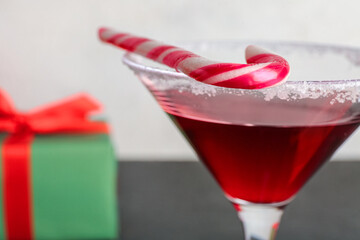 Glass of tasty red margarita with candy cane and Christmas gift on black table against white grunge background