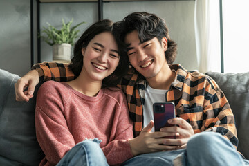 happy asian young couple using smart phone while relaxing on a couch in their living room at home