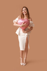 Beautiful young woman with heart-shaped balloon on brown background. Valentine's Day celebration