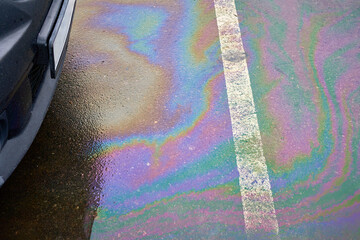 Leakage of oil or gasoline from the car on the asphalt in the parking lot.