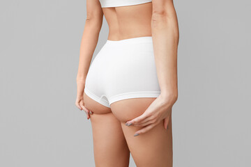 Young woman in panties on light background, back view. Plastic surgery concept