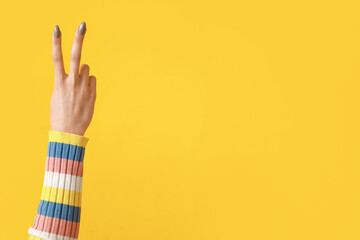 Fototapeta premium Young woman showing peace sign on yellow background